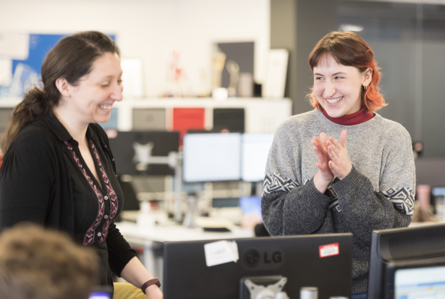 Two people smiling in an office together looking at a screen